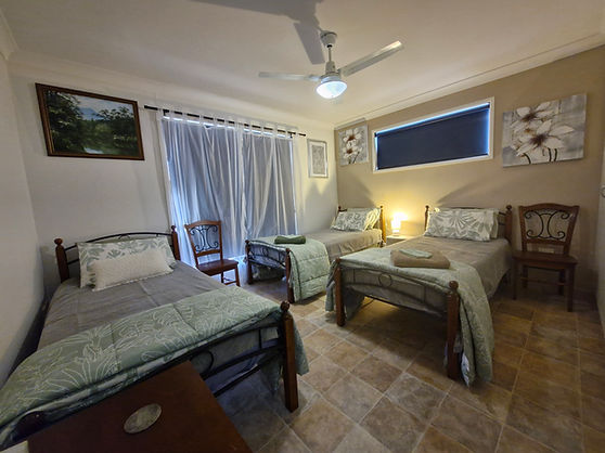 A hotel style room with three neatly made beds, placed side by side, with soft lighting and minimal decor Beulah Retreat