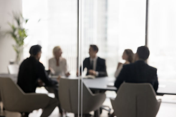 Group of businesspeople negotiating gathered in modern conference room, blurred silhouette