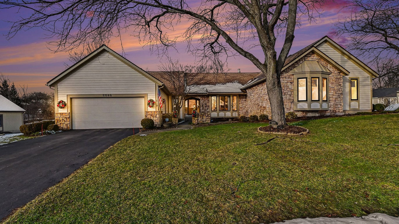 Ranch home at dusk with an attached garage and stone accents