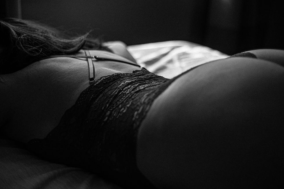 Monochrome close-up of a curvy woman lying face down on a bed wearing dark lace lingerie.