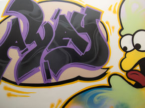 Ein Graffiti mit dem Namen der Jugendnotschlafstelle away, was von einer lustigen Banane ausgesprochen wird. Die Banane ist geb mit einer roten Zunge, die Farben des Namens sind schwarz mit lila Umrandung.