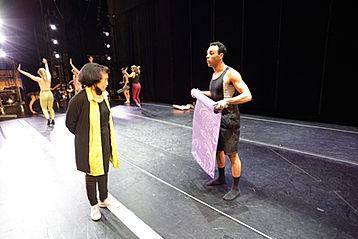 Baayork Lee and Samuel Colina in the middle of conversation. Samuel is rolling up a purple yoga mat and Baayork lee is wearing a yellow scarf.