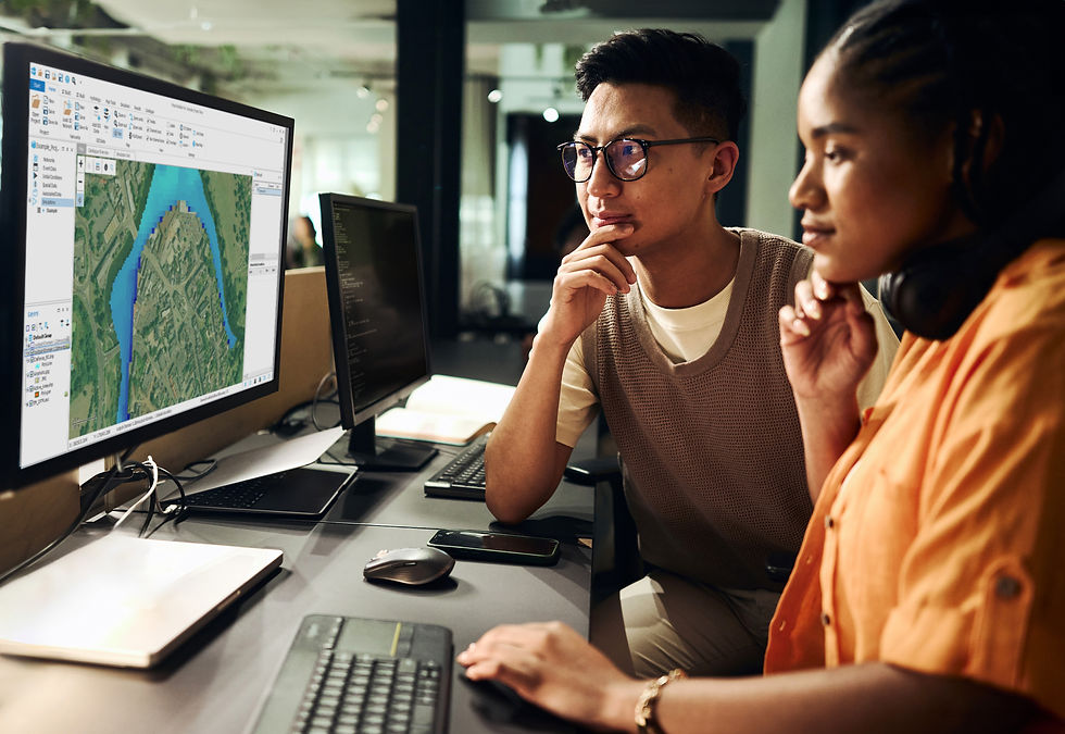 Two coworkers study a map on dual monitors in a modern office, one typing, both focused and thoughtful.