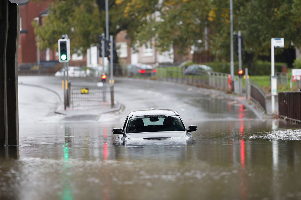 Car half-submerged in floodwater on a rainy street, with green and red traffic lights reflecting on the water.