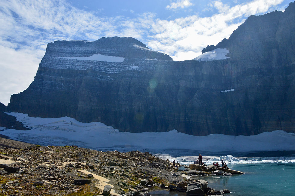 People along the shore of Grinnell Glacier Lake. Situated above and to the right of the people is Gem Glacier the smallest glacier in Glacier National Park