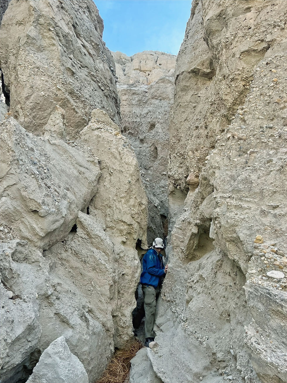 Hiker squeezing between walls of slot canyon in Mecca Hills