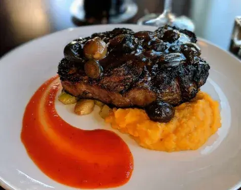 Plated steak with mushrooms, sweet potato purée, and red sauce