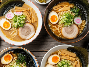 Four bowls of ramen with eggs, seaweed, and green onions on a wooden table. Side dishes include dumplings and pickles. Cozy and appetizing.