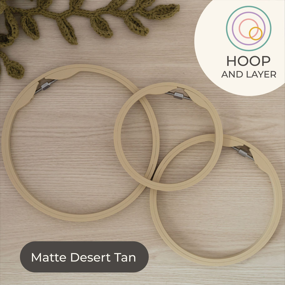 Set of three Matte Desert Tan round embroidery hoops on light wood background, styled with a green crochet plant