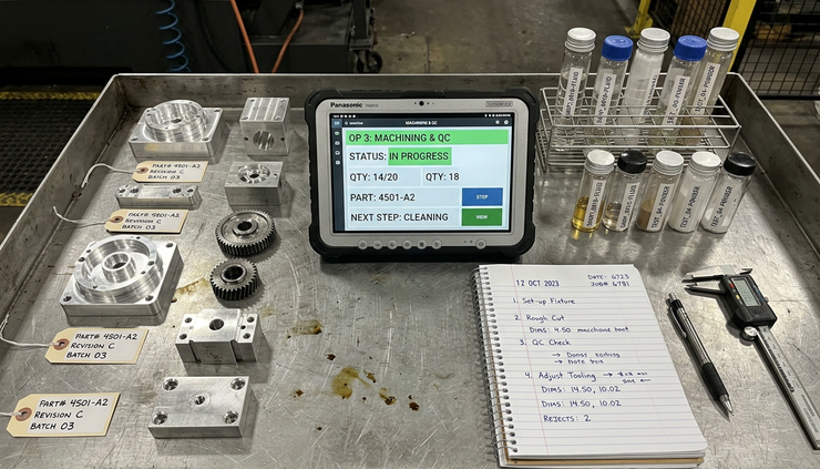 Overhead view of labeled metal parts and lab samples arranged beside a rugged tablet