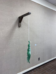 Clay sculpture of human frog hybrid holding onto rope. 