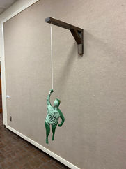 Clay sculpture of human frog hybrid holding onto rope. 