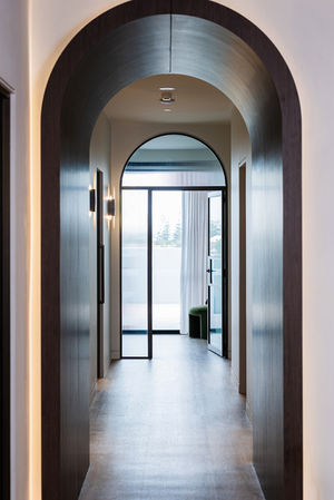 Modern hallway with arched deep timber doorway, wall lighting and fluted glass doors beyond.