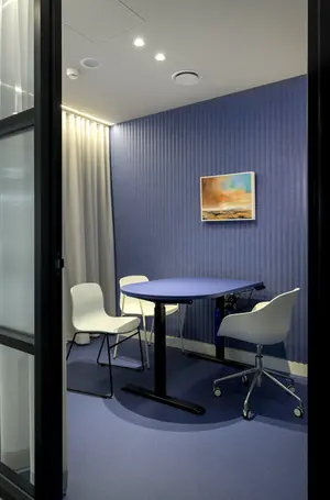 Small meeting pod with blue acoustic wall panelling walls and custom height adjustable desk.