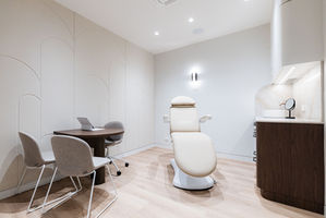 Modern, warm and inviting yet minimalist medical consulting room with white chair and timber laminate desk.