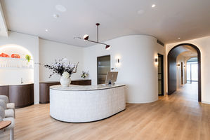 Modern medical reception area with curved walls, curved tiled desk and wooden floor.