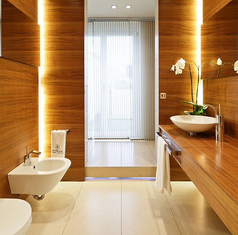 Innenarchitektonische Gestaltung und Planung eines exklusiven Gästebades mit WC, Bidet und Handwaschbecken. Wandverkleidung in Nussbaum mit integrierter Beleuchtung und Spiegel. Verchromte Armaturen von Jado für den exklusiven Geschmack und besondere Kundenwünsche. Boden aus Travertin Naturstein nach Fugenplan verlegt und mit individuellen Abmessungen, passend zu den Abmessungen des Raumes.