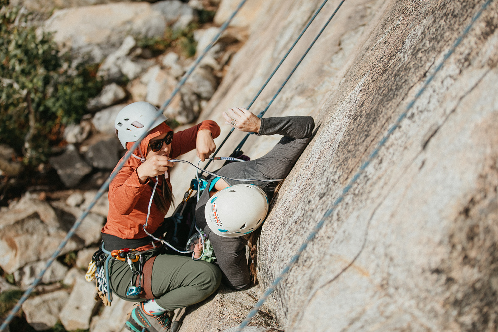 A helmeted course participant practices rope-system assistance beside a reclining climbing partner on granite