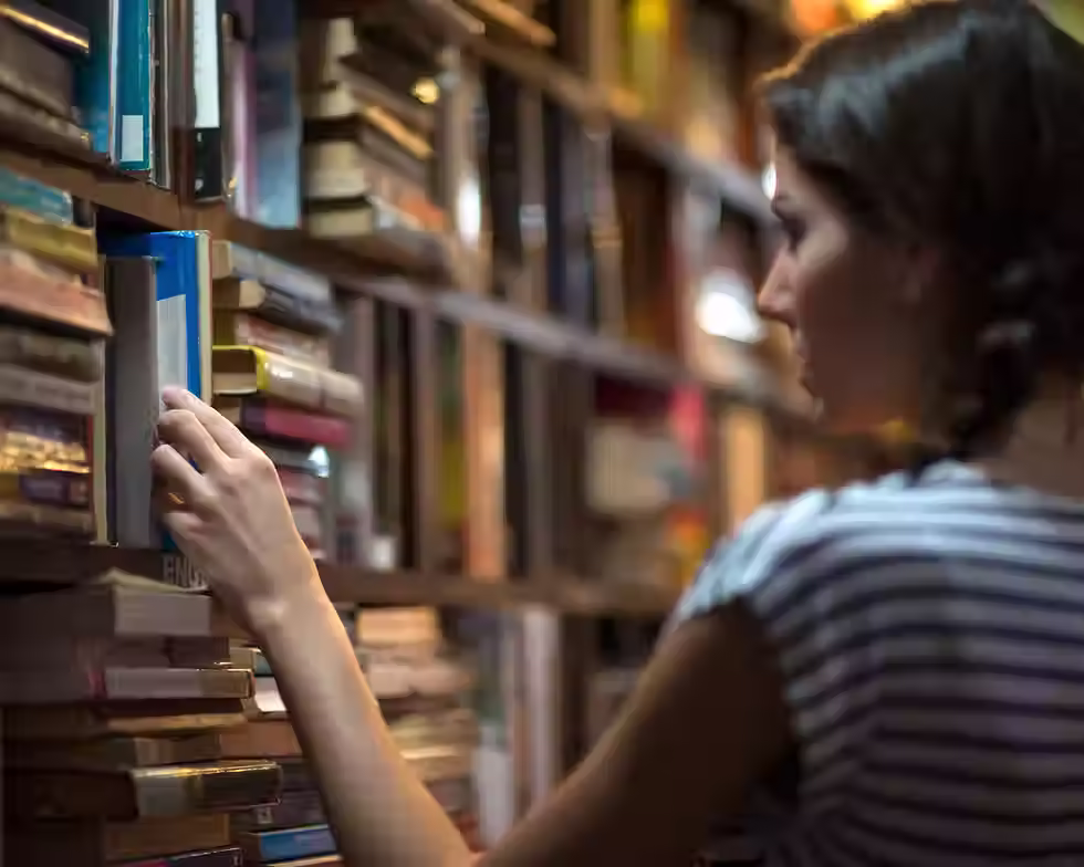 Читателка избира книга от препълнени рафтове в библиотека. Популярните бестселъри, трилъри и художествена литература предлагат на читателите безопасен начин да изследват човешката психология, реалните страхове и важни социални теми през разказите в книгите.