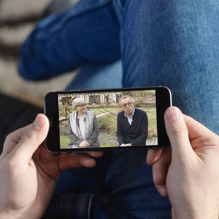 Une personne tient son smartphone et regarde une vidéo. Il s'agit d'une interview vidéo de Martine SAINT-LAURENT et Thierry PLOUVIER, réalisé dans le cadre de la promotion de l'événement Flaubert 2021