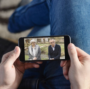 Une personne tient son smartphone et regarde une vidéo. Il s'agit d'une interview vidéo de Martine SAINT-LAURENT et Thierry PLOUVIER, réalisé dans le cadre de la promotion de l'événement Flaubert 2021