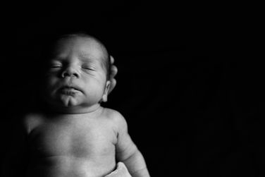 Photographie de naissance noire et blanc d'un bébé prise par Hugo Studio, photographe professionnel spécialisé dans la photographie de grossesse et de naissance en Normandie, Centre-Val de Loire et Île-de-France