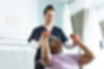diverse-senior-female-patient-exercising-with-weights-female-doctor-advising-hospital-room