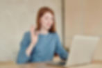 a young woman waving at a laptop monitor