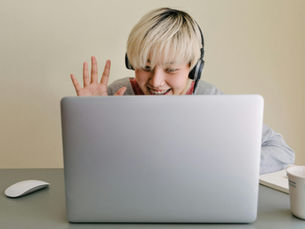 a young adult waving hello to a clinician they are meeting online on their laptop