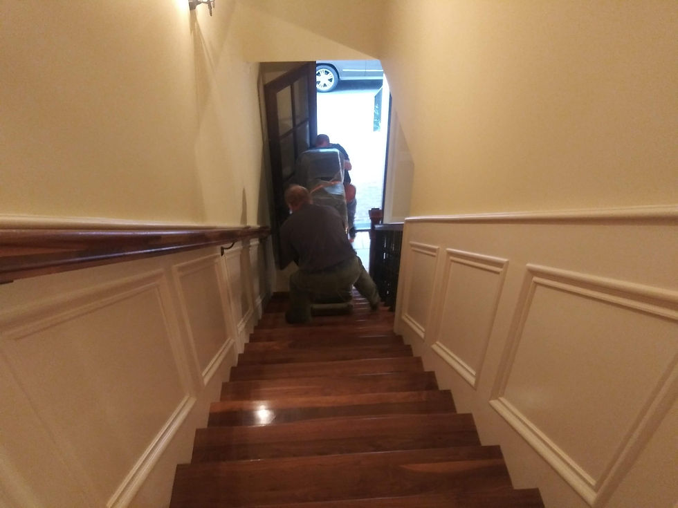 3 movers with a navy blue shirts with an ACME logo on them working together to move piano