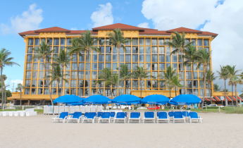 large yellow hotel venue with pblue umbrellas and chairs in frontal trees swaying and 