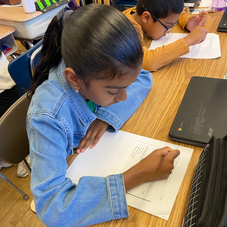 Female PS55Q students working next to laptop. She is doing paperwork on her desk.