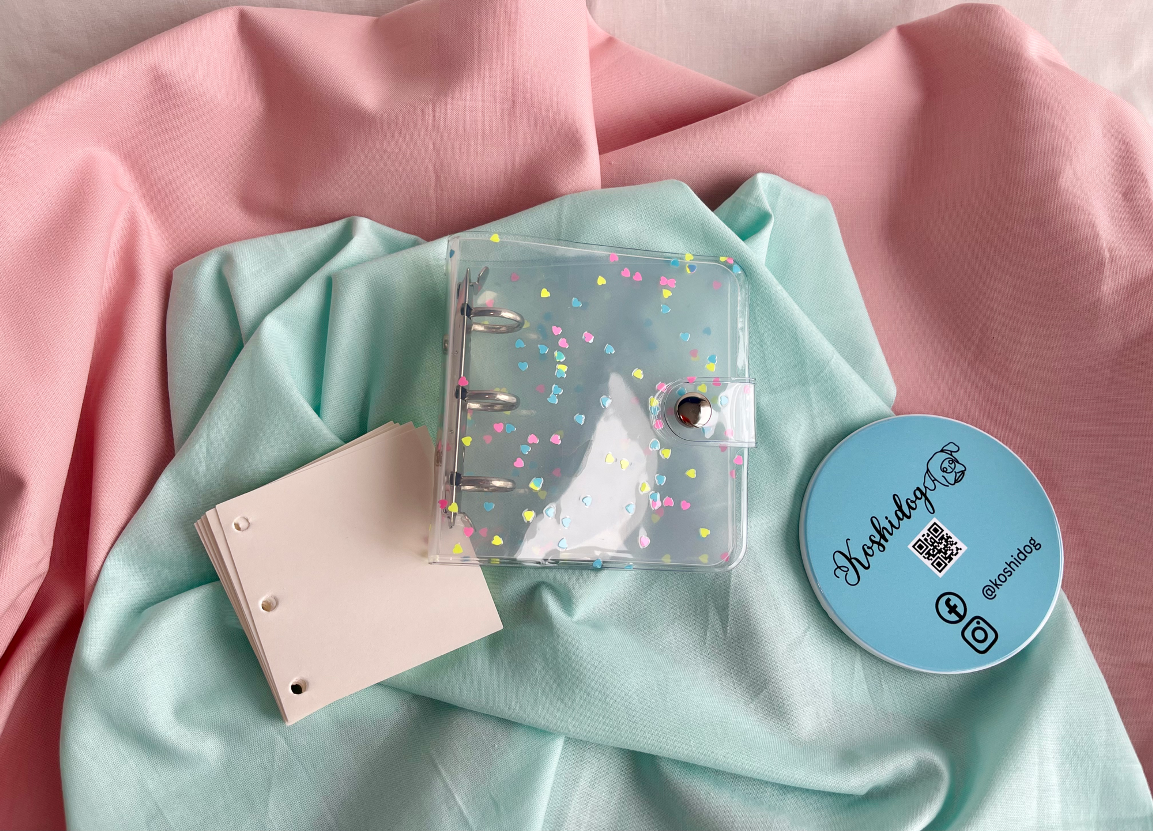 Tiny transparent mini binder with heart confetti design and clip closure.