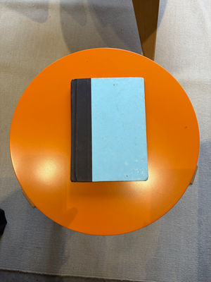 A closed blue and black book resting on a round orange table.