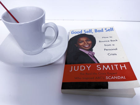 A white cup of coffee beside Judy Smith’s book Good Self, Bad Self on a white tabletop.