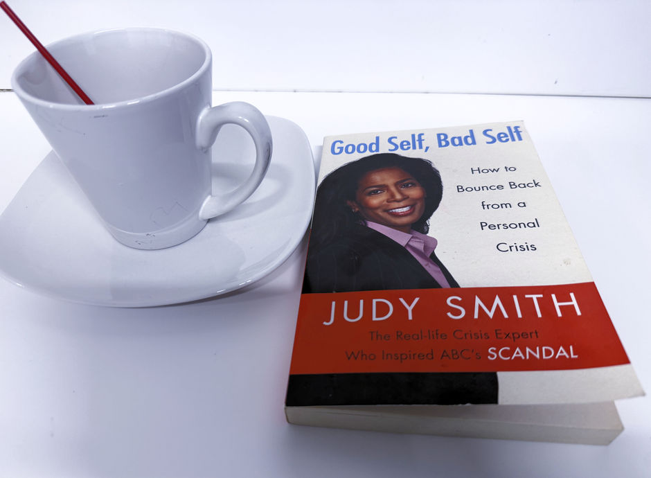 A white cup of coffee beside Judy Smith’s book Good Self, Bad Self on a white tabletop.