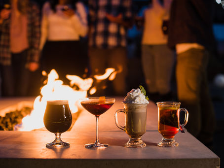 Group standing around a firepit drinking hot drinks, winter cocktails, and crisp beer