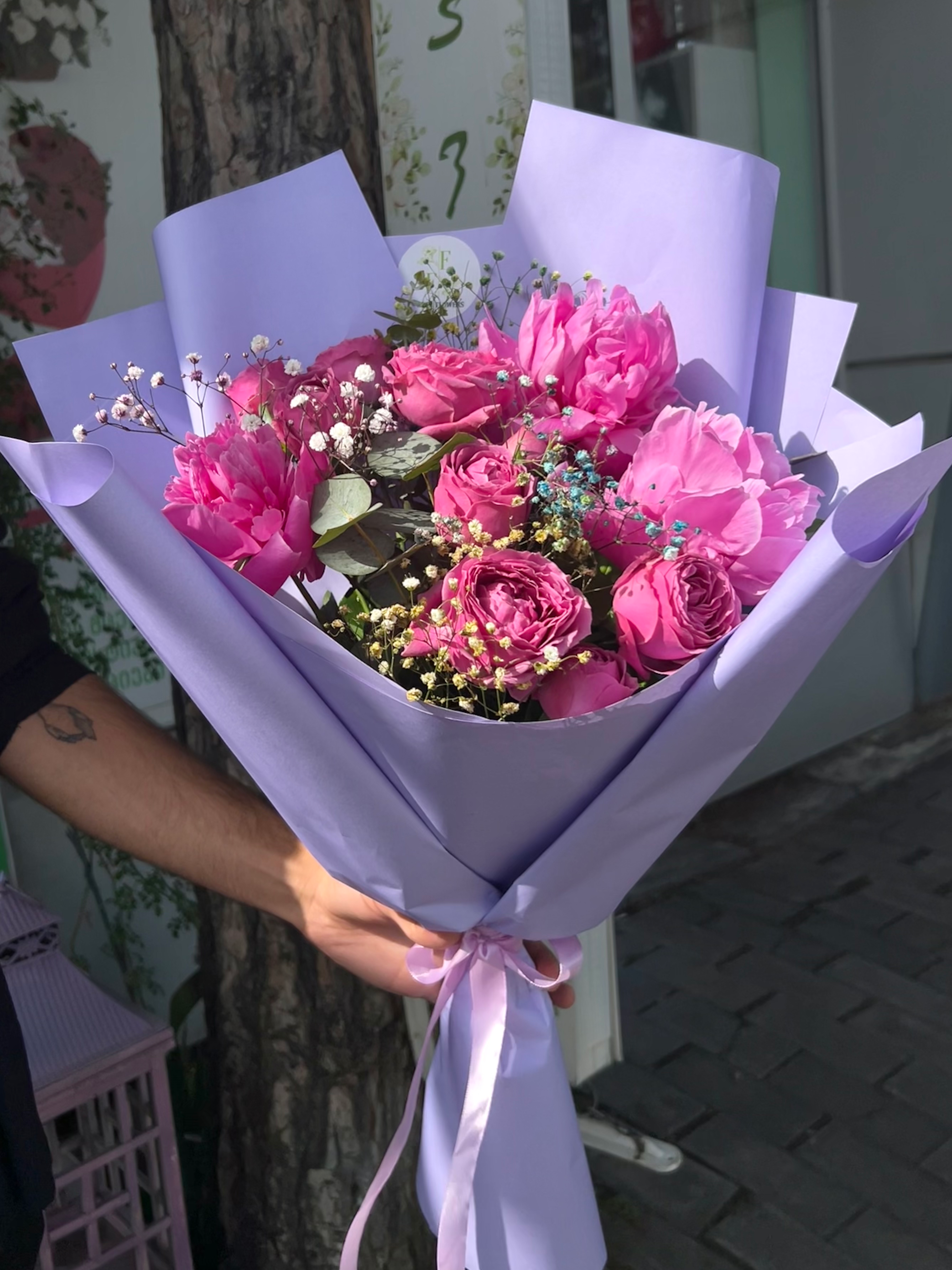 ვარდებისა და პიონების ლამაზი თაიგული იასამნისფერ შეფუთვაში