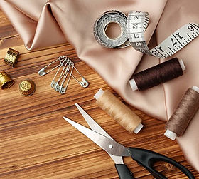 fabric, tape measure cotton, scissors, pins and thimble on a table