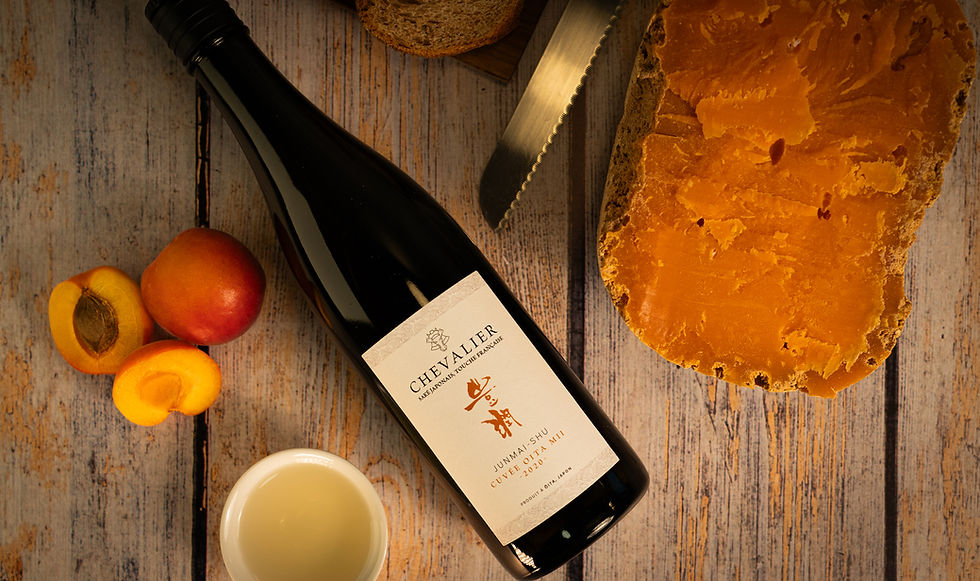 une table en bois avec dessus posé une bouteille de saké japonais, des abricots, de la mimolette et du pian au levain