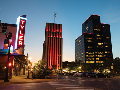 Downtown Tyler at dusk, featuring illuminated skyscrapers and the vibrant neon of the iconic Tyler Theater sign.
