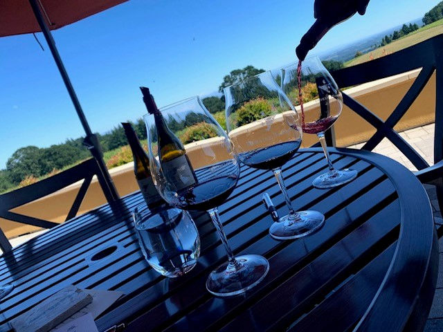 Red wine and glasses on an outdoor table overlooking the winery.