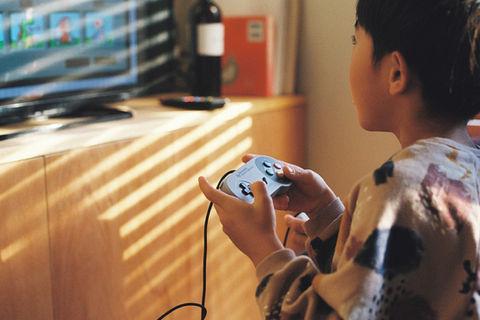 ゲームをする子供、テレビ画面に表示されるゲーム、コントローラーを持つ手元、背景に木製家具