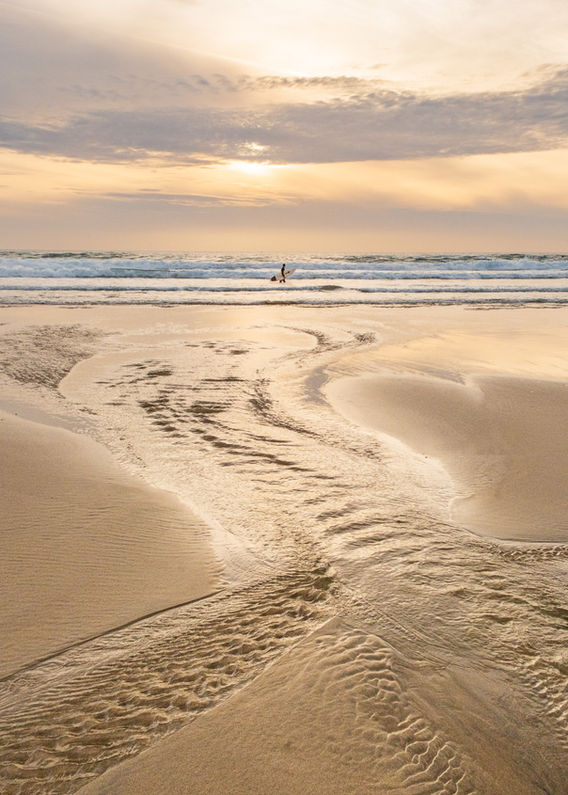River flowing into sea at sunset with surfer