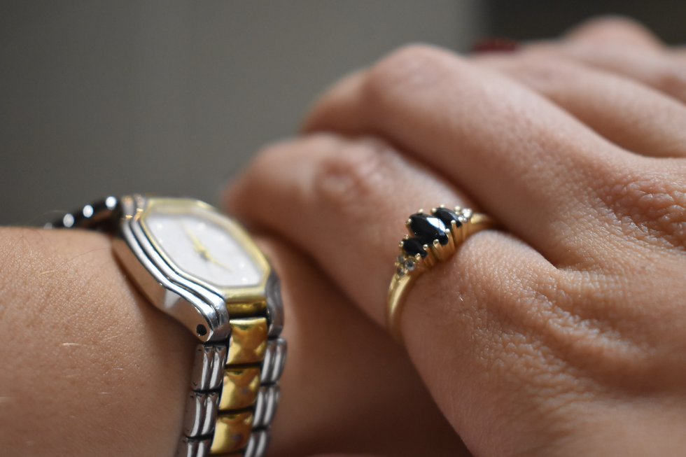 Picture of a hand with a gold ring and black stones holding onto a hand with a silver and gold watch