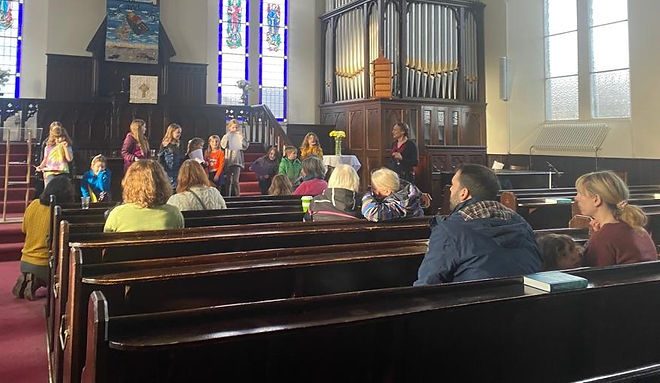 Messy Church in Belhaven Church with adults and children, some sitting in pews and some standing at the front