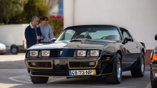 Famílias e entusiastas reunidos junto a automóveis clássicos no parque, celebrando o Dia da Mulher em ambiente festivo