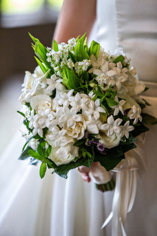 A bride holding her custom wedding bouquet full of white flowers with occasional small purple accents.