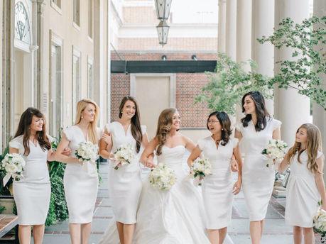 A bride and her bridal party, all dressed in white, holding their custom bouquets and smiling.