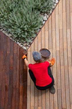 A worker painting wooden deck with protective decking oil bucket top view